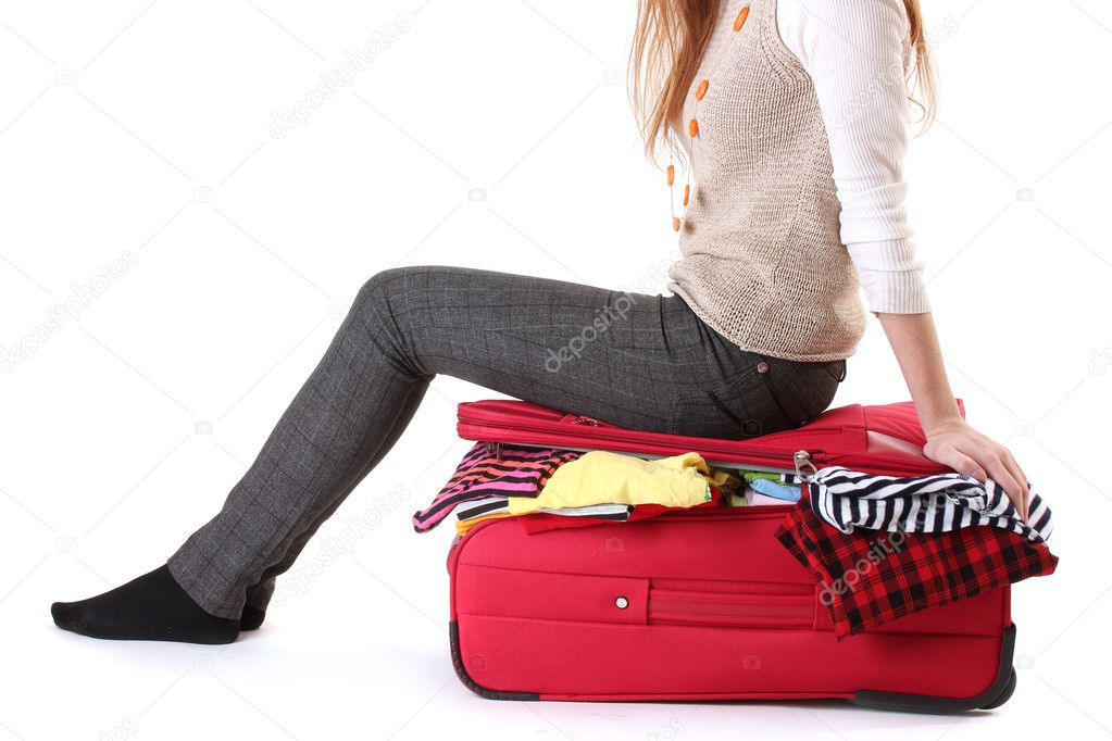Girl sitting on a suitcase and tries close it isolated on a white
