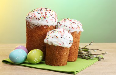 Beautiful Easter cakes, colorful eggs and pussy-willow twigs on wooden table on green background clipart