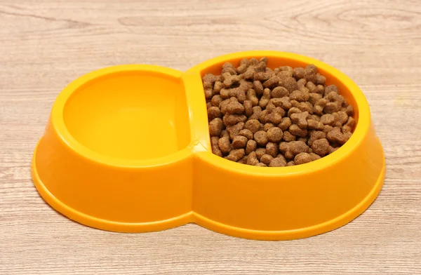 Comida de gato seco e água em tigela amarela no fundo de madeira — Fotografia de Stock