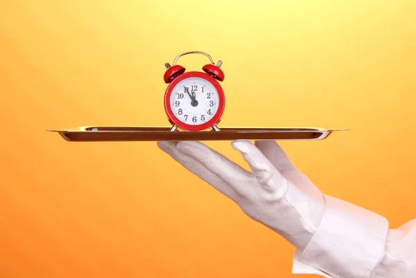 stock image Hand in glove holding silver tray with alarm clock on yellow background