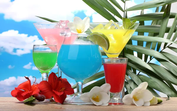 Exotische cocktails en bloemen op tafel op blauwe hemelachtergrond — Stockfoto