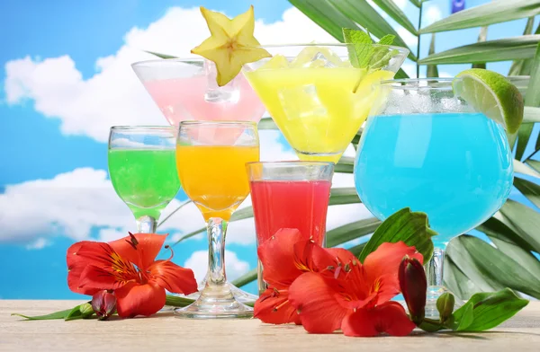 Exotische Cocktails und Blumen auf dem Tisch vor blauem Himmel Hintergrund — Stockfoto