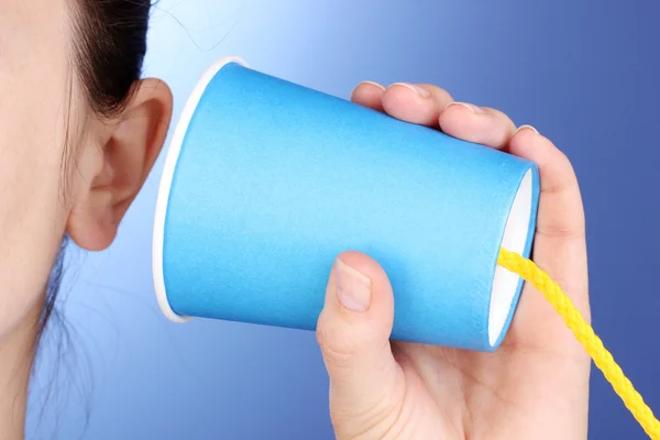 Человеческое ухо и бумажная чашка рядом с ним крупным планом на синем фоне — стоковое фото