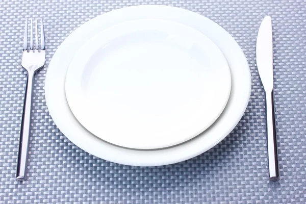 Bílé prázdné talíře, vidličku a nůž na šedé ubrus — Stock fotografie
