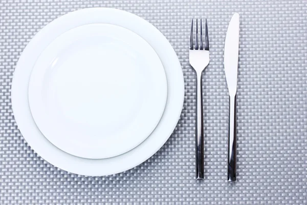 Placas brancas vazias com garfo e faca em uma toalha de mesa cinza — Fotografia de Stock