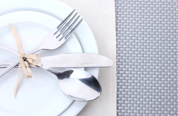 stock image White empty plates with fork, spoon and knife tied with a ribbon on a grey tablecloth