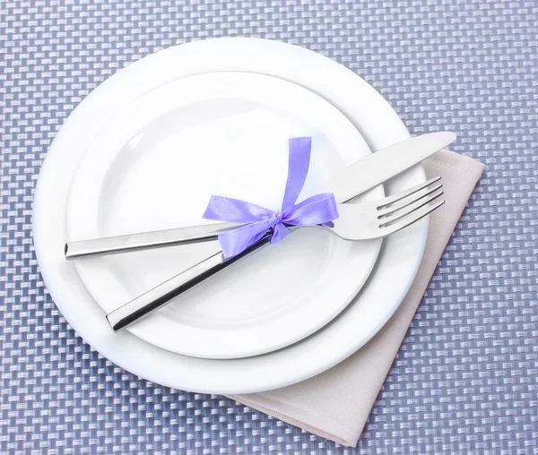 Weiße leere Teller mit Gabel und Messer, die mit einer Schleife auf einer grauen Tischdecke gebunden sind — Stockfoto