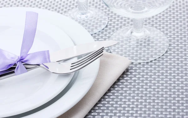 Piatti bianchi vuoti, forchetta e coltello legati con un nastro e bicchieri su una tovaglia grigia — Foto Stock