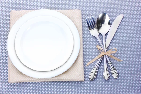 Piatti bianchi vuoti con forchetta, cucchiaio e coltello legati con un nastro su una tovaglia grigia — Foto Stock