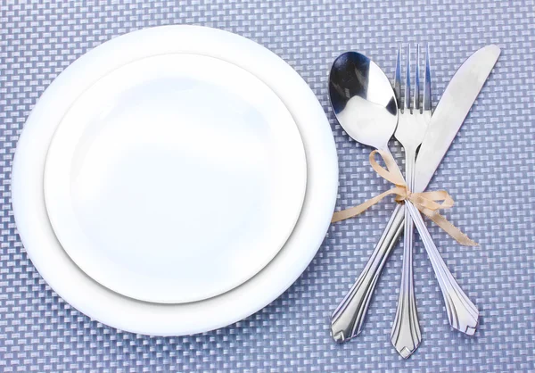 Белые пустые тарелки с вилкой, ложкой и ножом, завязанные лентой на серой скатерти — стоковое фото