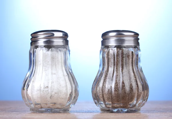 Sůl a pepř mlýny na dřevěný stůl na modrém pozadí — Stock fotografie