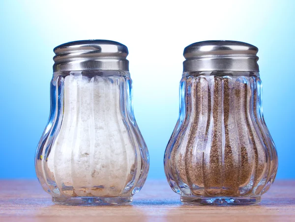 Molinos de sal y pimienta sobre mesa de madera sobre fondo azul —  Fotos de Stock