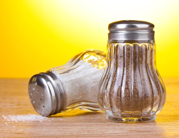 Salt and pepper mills on wooden table on yellow background — Stock Photo, Image
