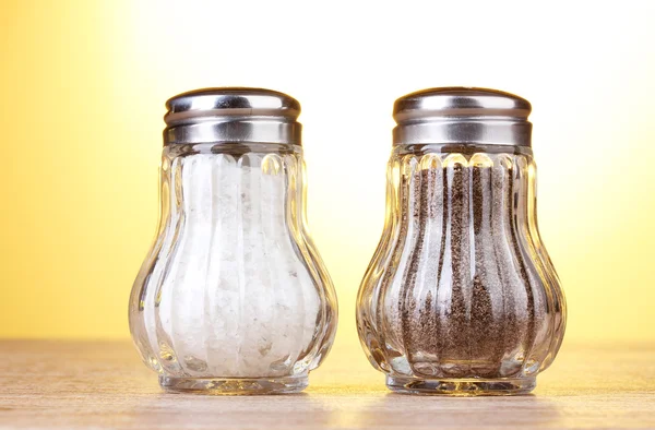 Αλάτι και πιπέρι νερόμυλους στην ξύλινο τραπέζι σε κίτρινο φόντο — Φωτογραφία Αρχείου