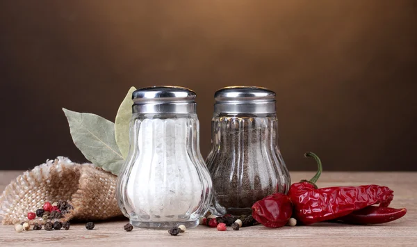 stock image Salt and pepper mills and spices on wooden table on brown background