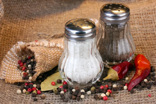 Salt and pepper mills and spices on burlap background — Stock Photo, Image