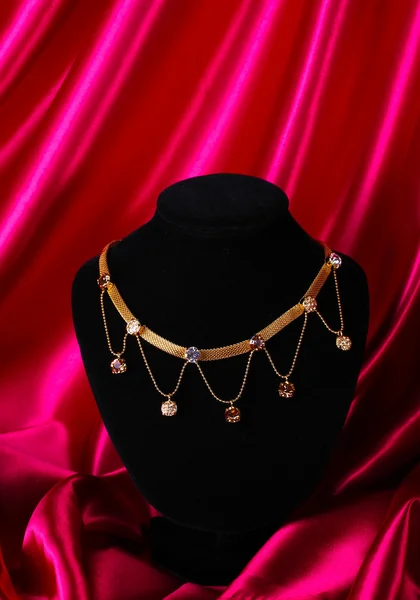 Hermoso collar de oro en el maniquí en tela de seda roja — Foto de Stock