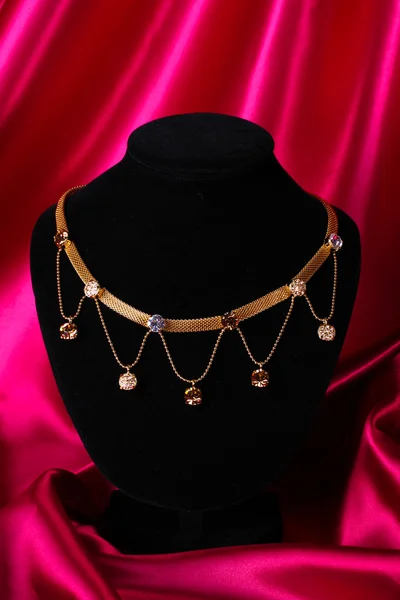 Belo colar dourado no manequim no tecido de seda vermelho — Fotografia de Stock
