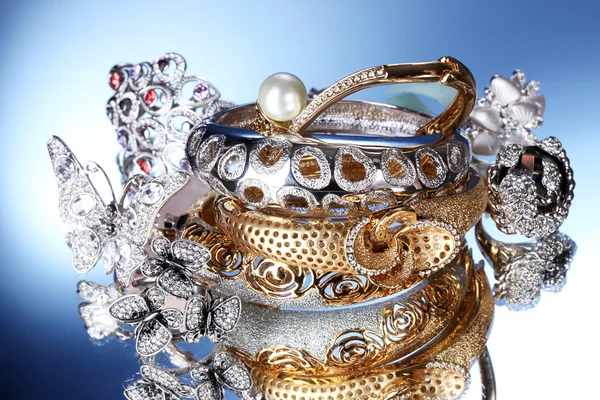 Hermosas pulseras y anillos de plata y oro sobre fondo azul — Foto de Stock