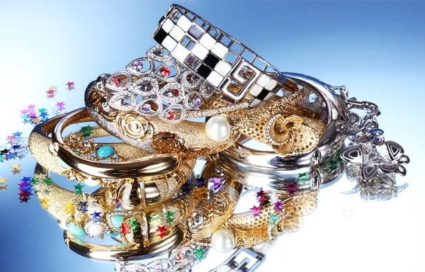 Hermosas pulseras y anillos de plata y oro sobre fondo azul — Foto de Stock