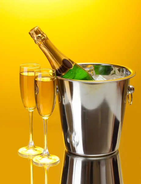 Champagne bottle in bucket with ice and glasses of champagne, on yellow background — Stock Photo, Image