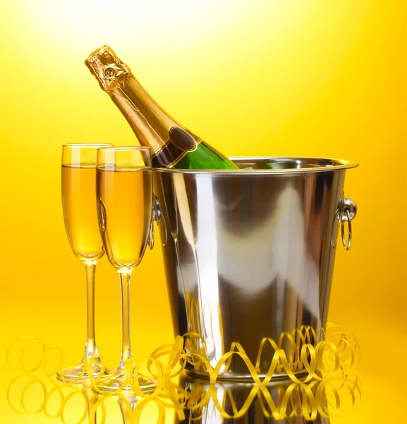 Bouteille de champagne dans un seau avec glace et verres de champagne, sur fond jaune — Photo