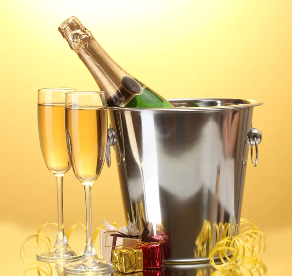 Botella de champán en cubo con hielo y copas de champán, sobre fondo amarillo — Foto de Stock