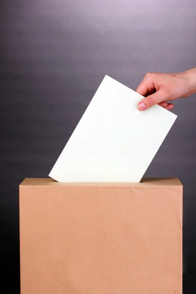 Hand mit Wahlzettel und Urne auf grauem Hintergrund — Stockfoto