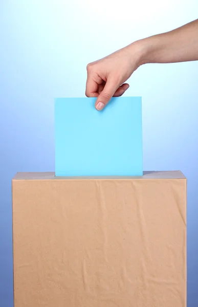 Mão com cédula de voto e caixa no fundo azul — Fotografia de Stock