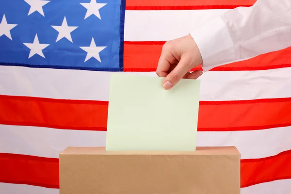 Main avec bulletin de vote et urne sur Drapeau des États-Unis — Photo
