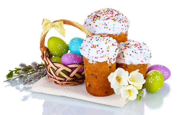 Piękne wielkanocne ciasta, kolorowe jajka w koszyku i kwiaty na białym tle — Zdjęcie stockowe