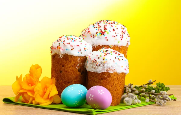 Hermosos pasteles de Pascua, huevos coloridos y ramitas de coño y sauce en la mesa de madera sobre fondo amarillo —  Fotos de Stock