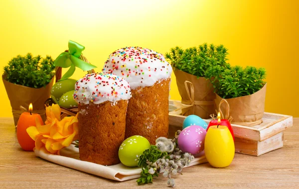 Красивые пасхальные торты, красочные яйца и свечи на деревянном столе на желтом фоне — стоковое фото