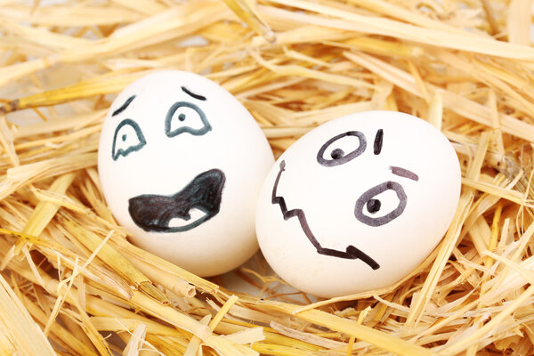 Белые яйца со смешными лицами в соломе
