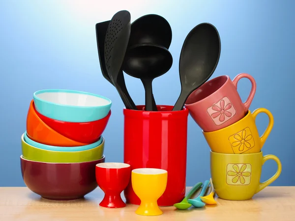 Ciotole vuote luminose, tazze e utensili da cucina su tavolo in legno su sfondo blu — Foto Stock