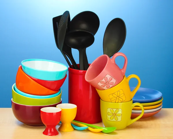 Яркие пустые миски, чашки и кухонные принадлежности на деревянном столе на синем фоне — стоковое фото