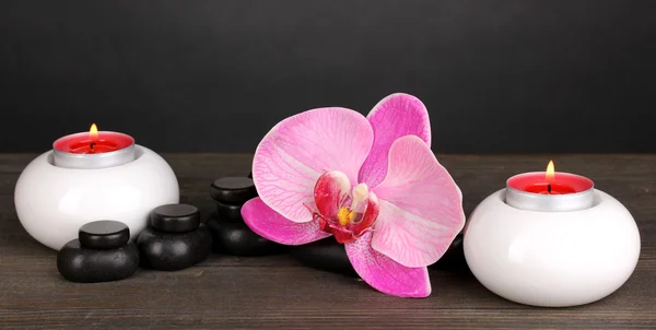 Wellness kameny s orchidej květina a svíčky na dřevěný stůl na šedém pozadí — Stock fotografie