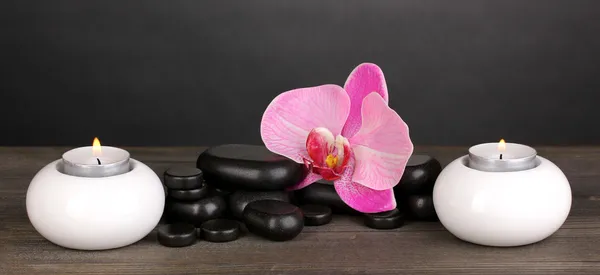 蘭の花とグレーの背景上の木製のテーブルの上のろうそくスパ石 — ストック写真