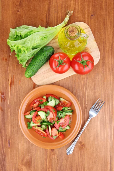 Verse salade met tomaten en komkommers op houten achtergrond — Stockfoto