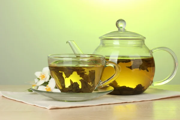 Зелений чай з жасмином в чашці і чайник на дерев'яному столі на зеленому фоні — стокове фото