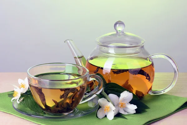 Grøn te med jasmin i kop og tekande på træbord på grøn baggrund - Stock-foto