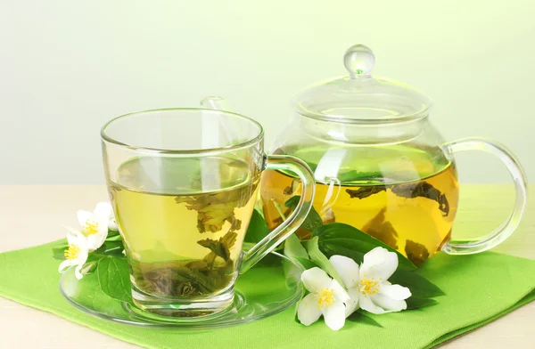 Зелений чай з жасмином в чашці і чайник на дерев'яному столі на зеленому фоні — стокове фото