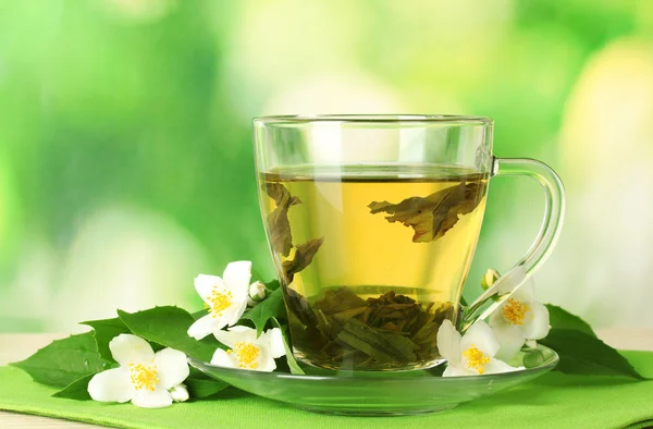 Csésze zöld tea, jázmin virágok, a zöld háttér fából készült asztal — Stock Fotó