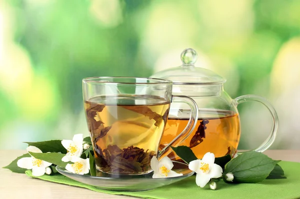 Grüner Tee mit Jasmin in Tasse und Teekanne auf Holztisch auf grünem Hintergrund — Stockfoto