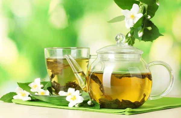 Grüner Tee mit Jasmin in Tasse und Teekanne auf Holztisch auf grünem Hintergrund — Stockfoto