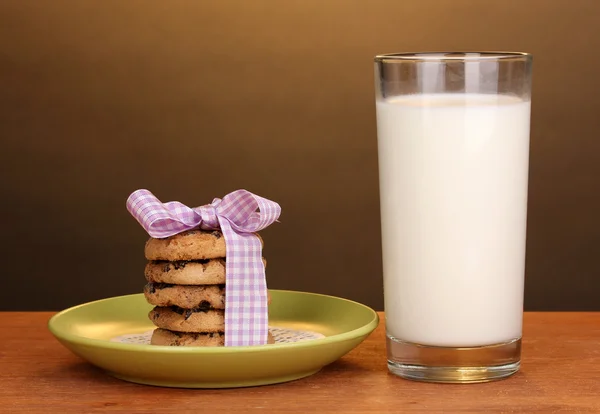 Glass of milk and cookies on wooden table on brown background — Stock Photo, Image