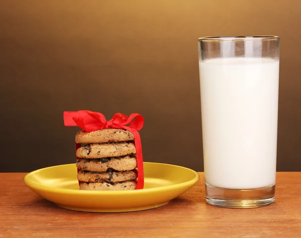 Copo de leite e biscoitos na mesa de madeira no fundo marrom — Fotografia de Stock