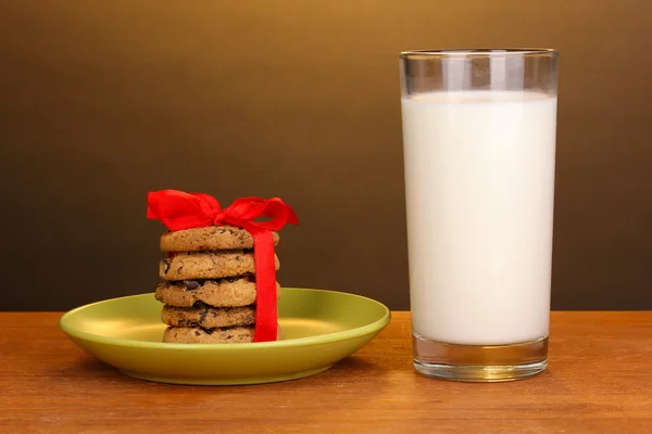 Стакан молока и печенья на деревянном столе на коричневом фоне — стоковое фото