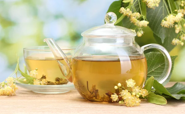 Tetera y taza con té de tilo y flores en la mesa de madera en el jardín —  Fotos de Stock