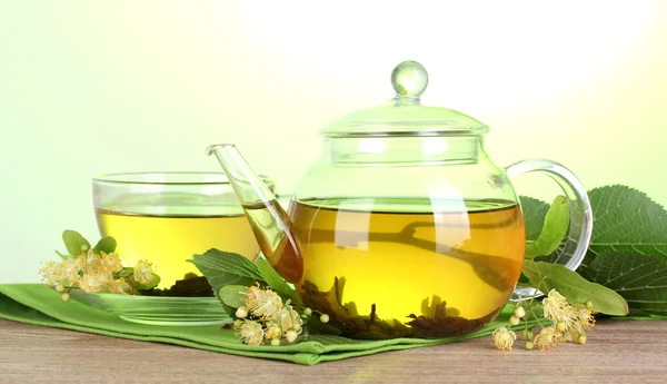 Teáskanna és a csésze linden tea és a virágok, a zöld háttér fából készült asztal — Stock Fotó